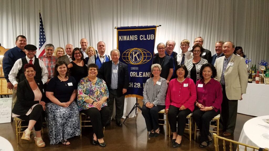 standing and seated members of the local New Orleans Kiwanis group in front of their flag