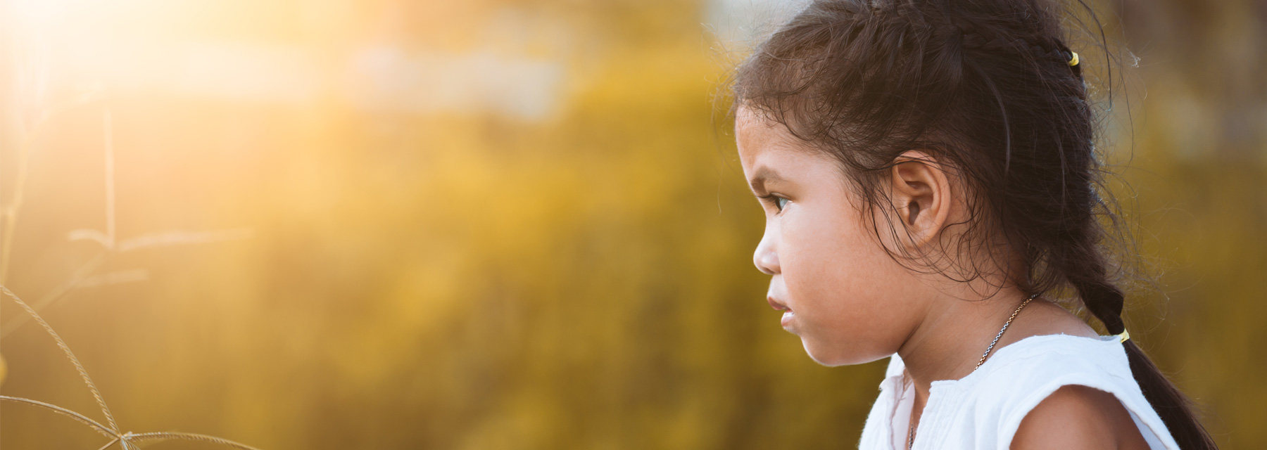 Young girl with brown hair and white sleeveless sun dress watching the sunset in a golden wheat field