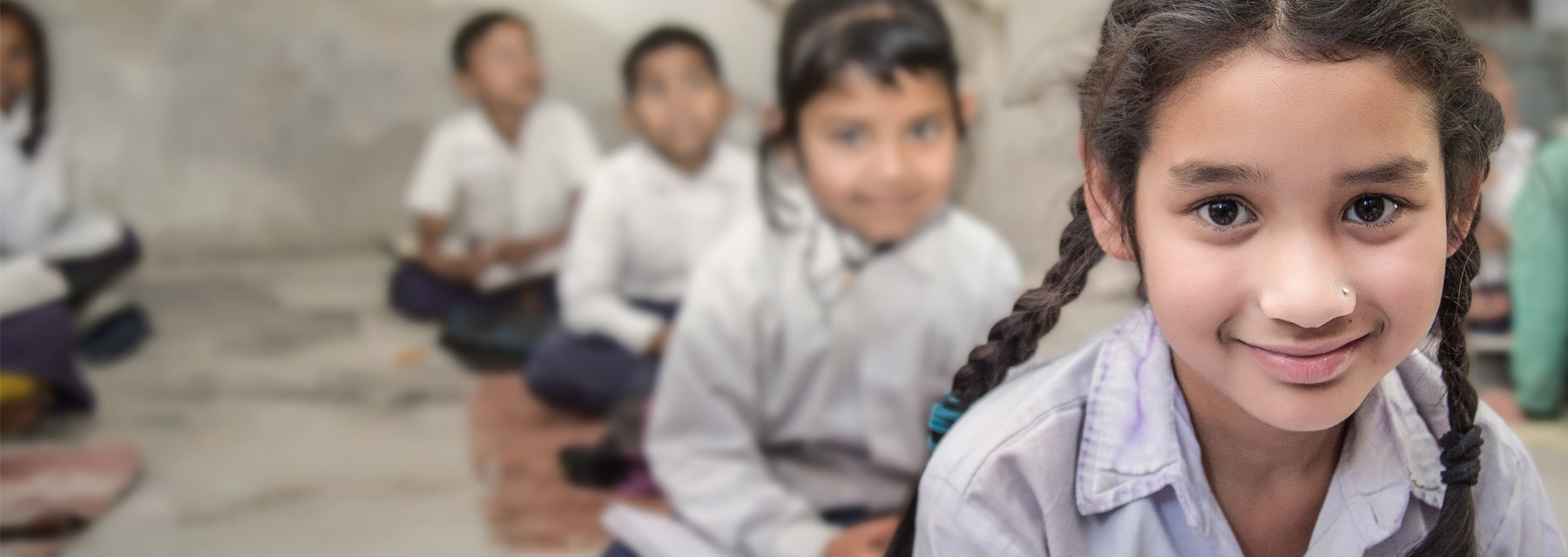 Young children in white and blue school uniforms sitting in classroom on the floor on rugs