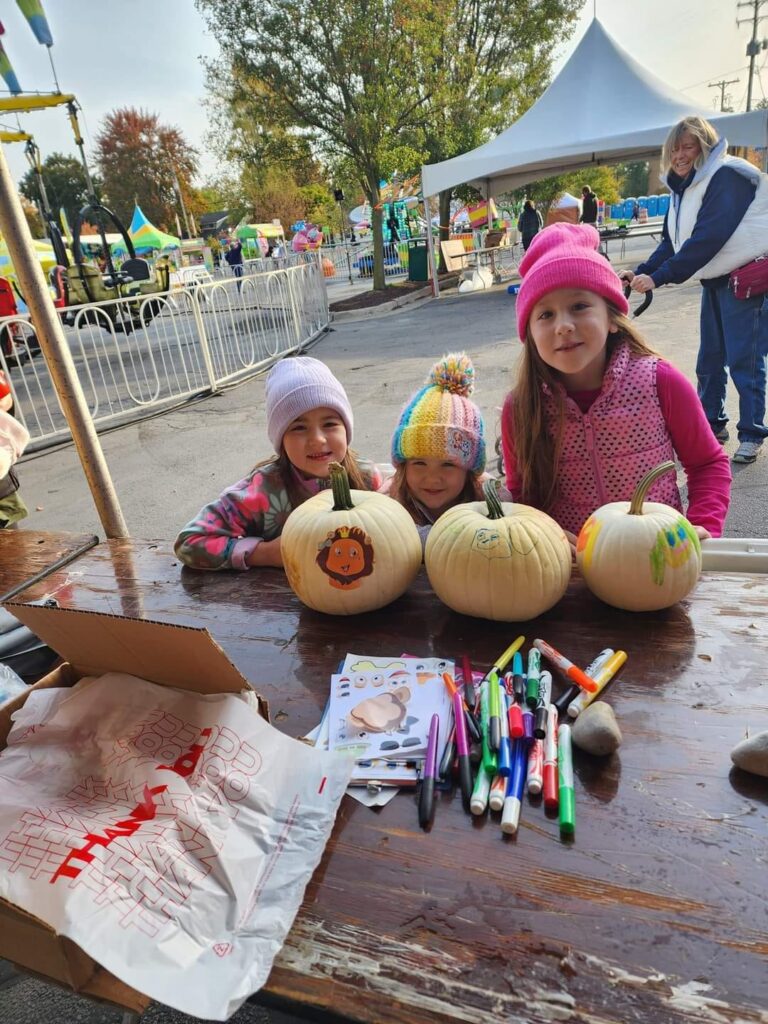 Three children pose with their decorated pumpkins at Kiwanis Club of Tecumseh's Make-it Take-it booth during Appleumpkin