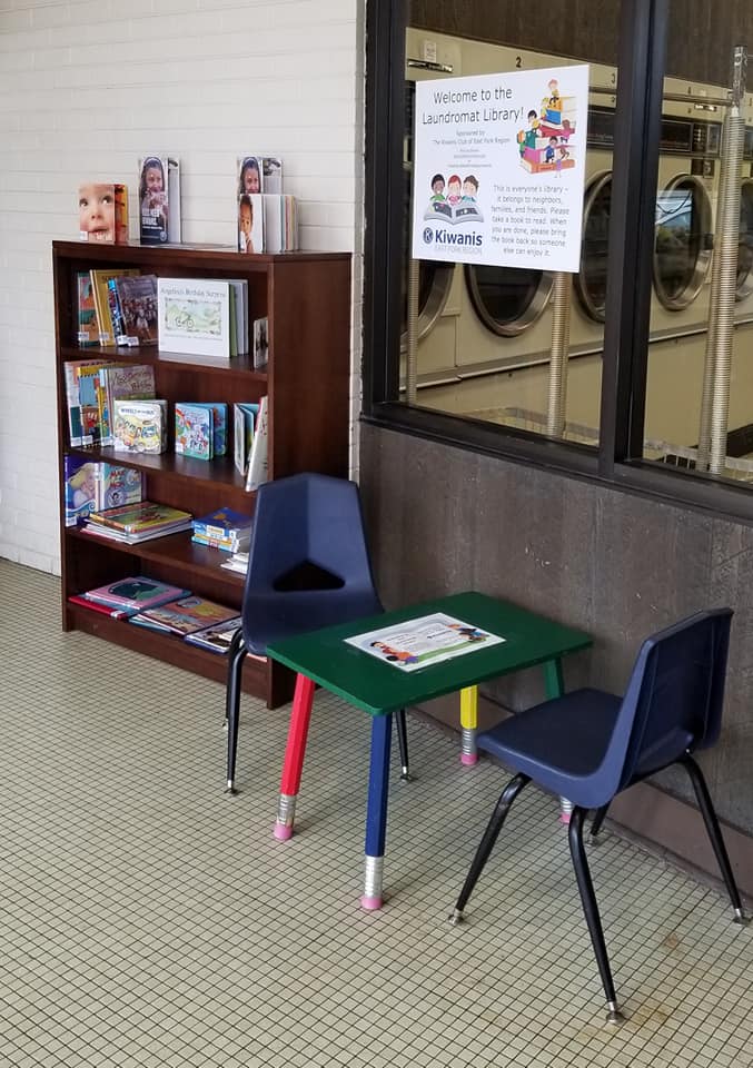 Book shelf with children's books, table and chairs, and Laundromat Library sign