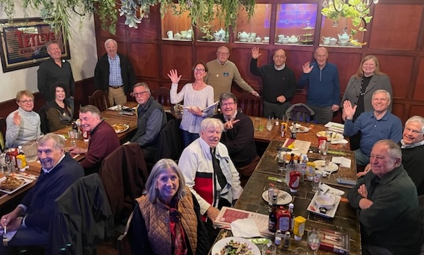 Image of members of Kiwanis Club of North Shore Milwaukee meeting in a restaurant meeting room and waving to the camera.