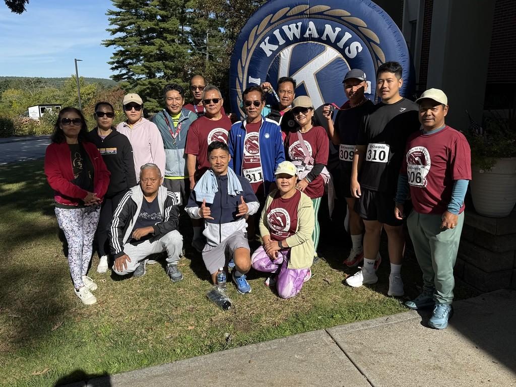 A group of about twenty runners, many in matching maroon shirts, gathers for a photo in front of the inflatable Kiwanis logo.