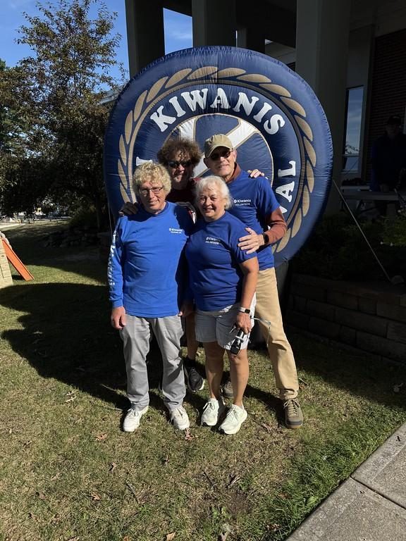 Three Kiwanis volunteers in blue shirts smile in front of a large inflatable Kiwanis International logo.