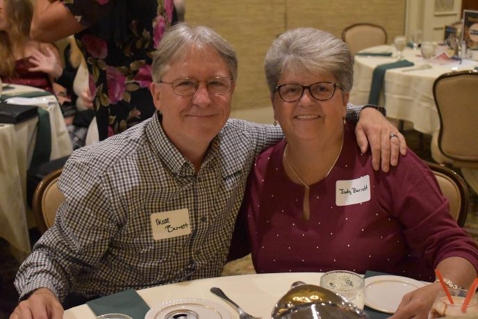 A smiling couple wearing name tags seated together at a dinner table at the gala.