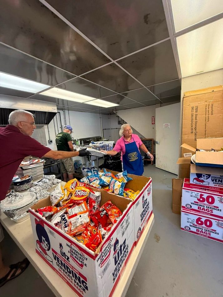 Volunteers at a serving station with a large box full of individual chip bags.