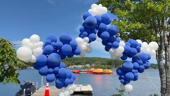 A blue-and-white balloon arch on a dock, framing a row of colorful rafts on the lake.