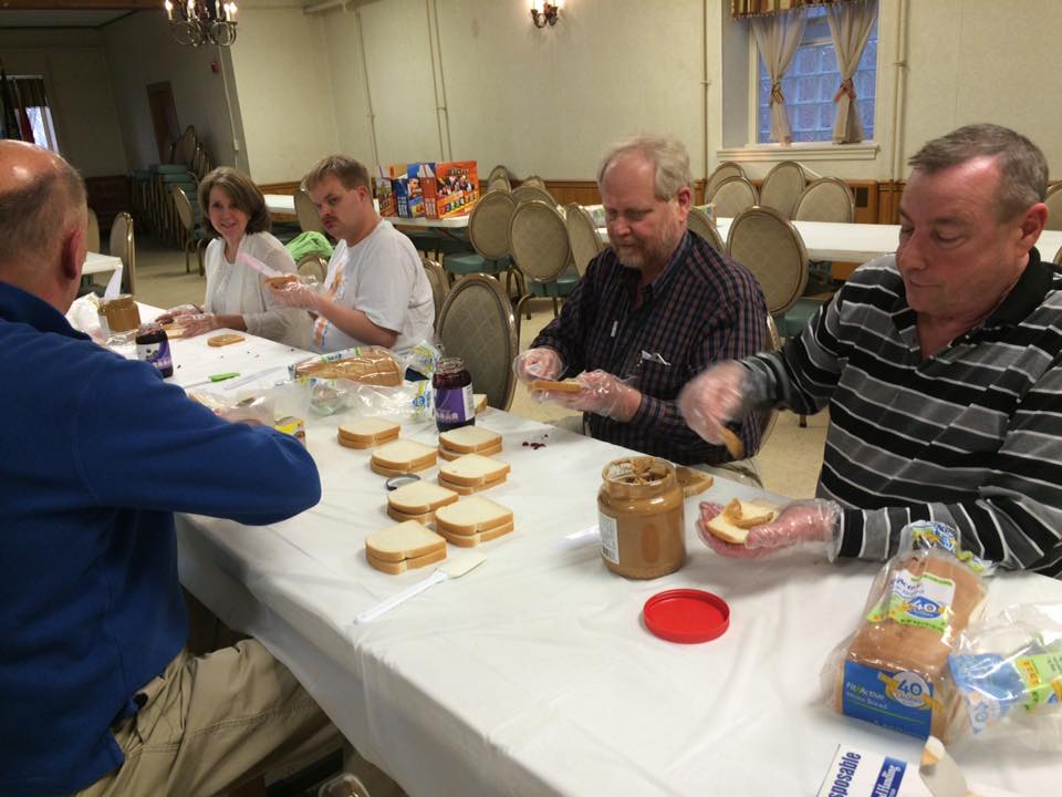 Members sitting at long table making peanut butter and jelly sandwhiches