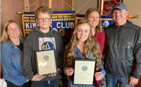 Two middle school students, one male and one female, holding certificates with their parents standing next to them.