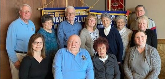 Two rows of people of various ages. Four seated in the front and eight standing behind facing the camera and smiling.