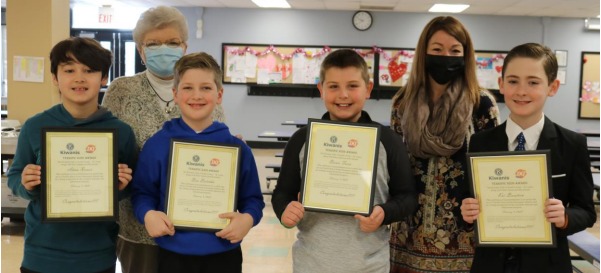 Four elementary school students holding certificates along with their principal and Kiwanis sponsor.