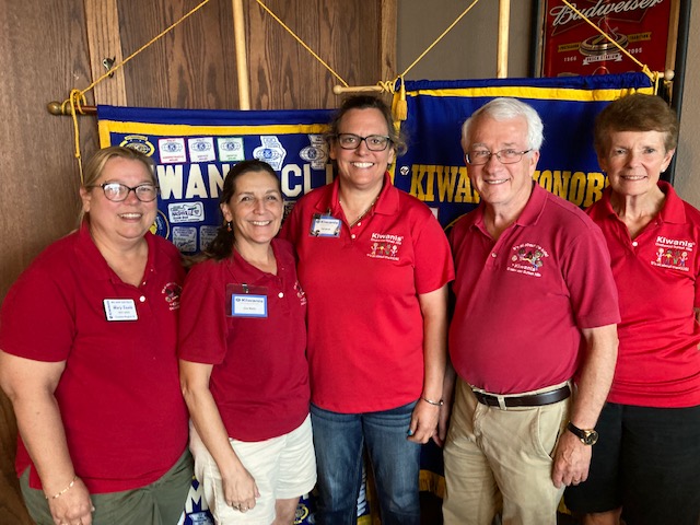 4 adults in red shirts stand in front of the club flags