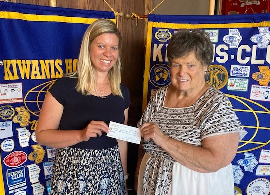 Two women stand in front of blue flags and hold a check