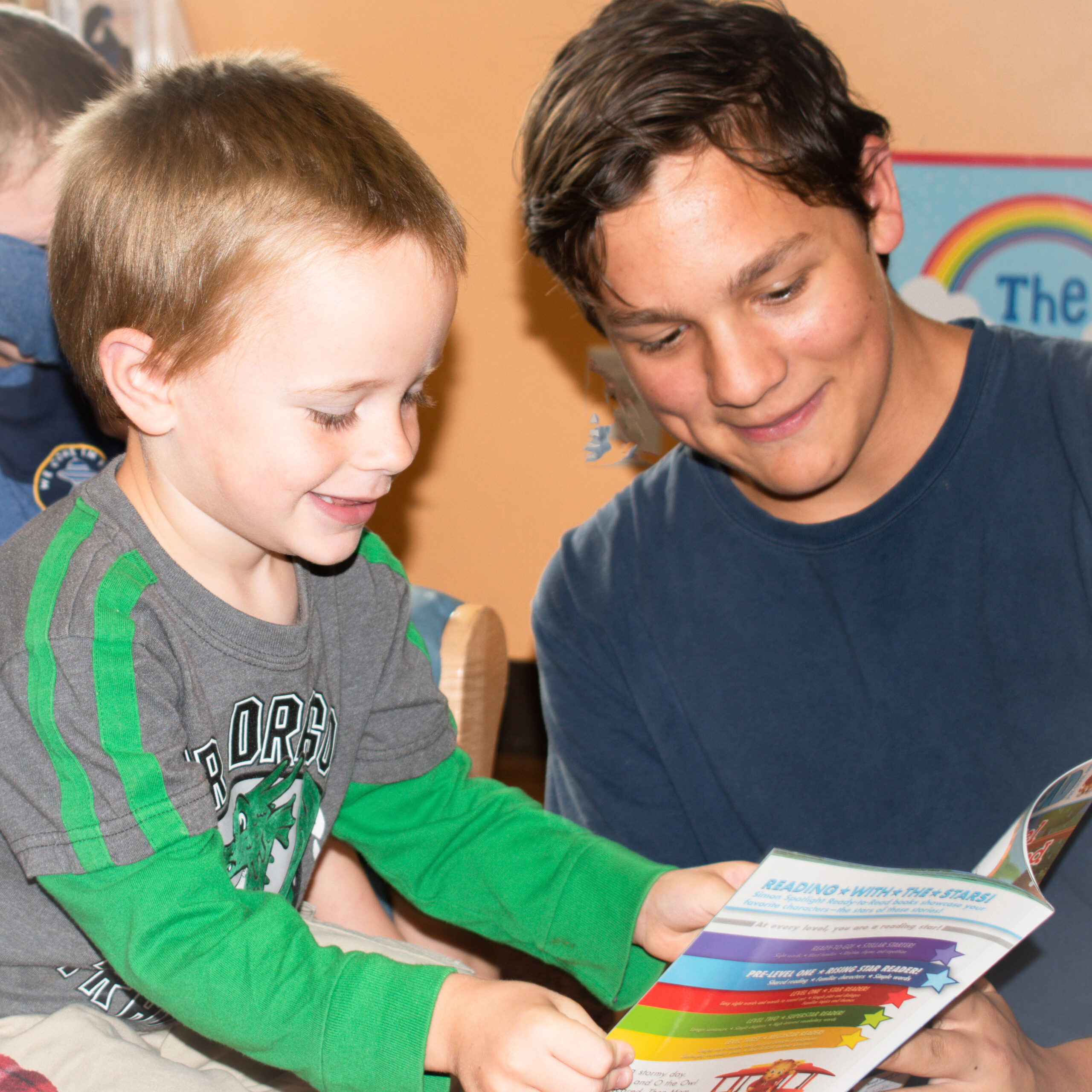 A high school student and a young child read a book together