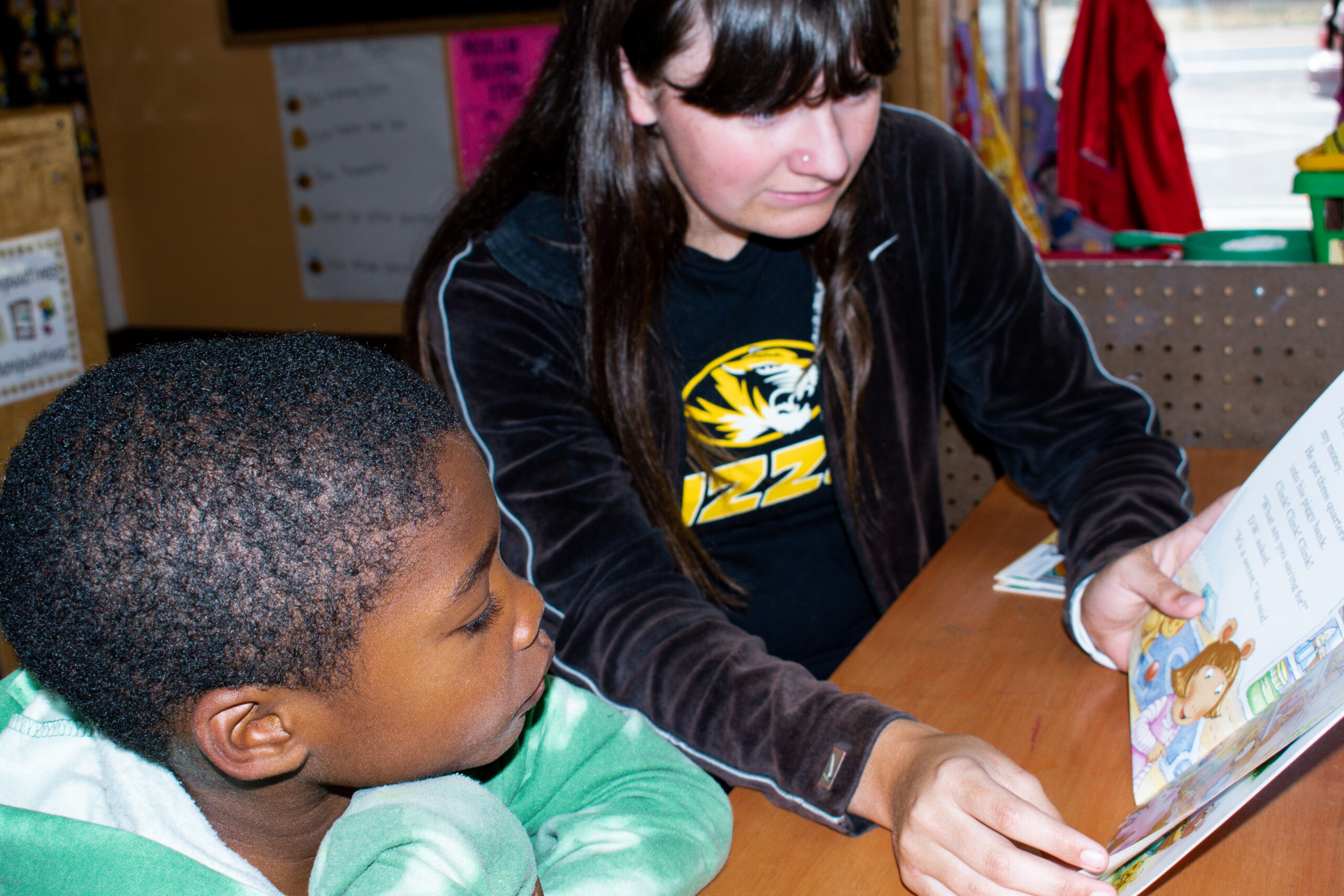 A high school student and a young child read a book together