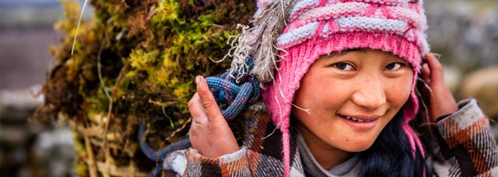 Young nepalese girl smiling with pink wool hat carrying a woven basket full of vegetables
