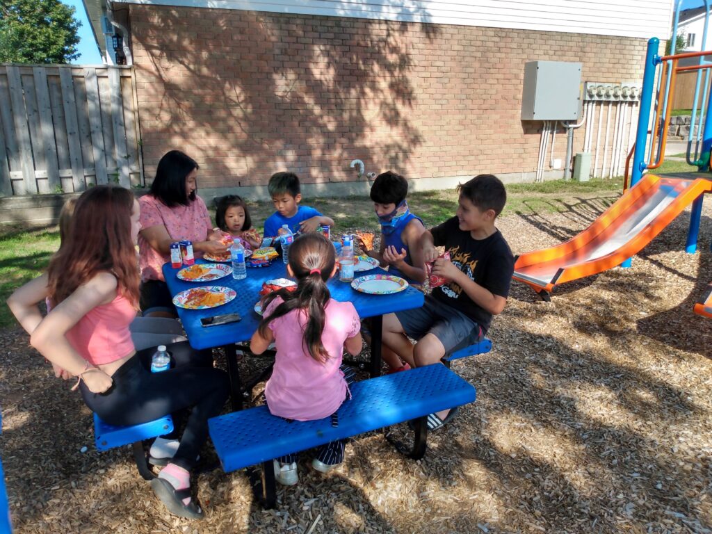 Residents of K-W Kiwanis affordable housing enjoy free pizza on a sunny day  in their colourful new playground