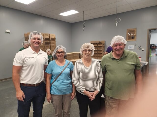 Four people wearing packing bonnets in the food packing room at Feed My Starving Children