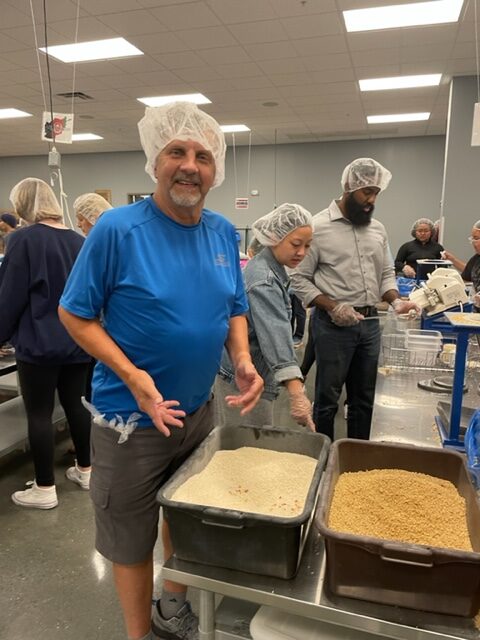 Man wearing head bonnet during food packing event at Feed My Starving Children, showing bins of food being packed