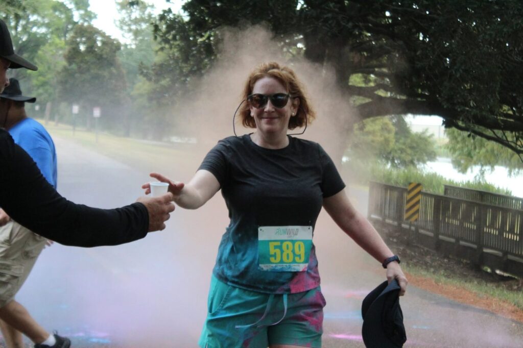 Runner wearing bib 589 gets a high five at a color station as blue and pink powder fills the air