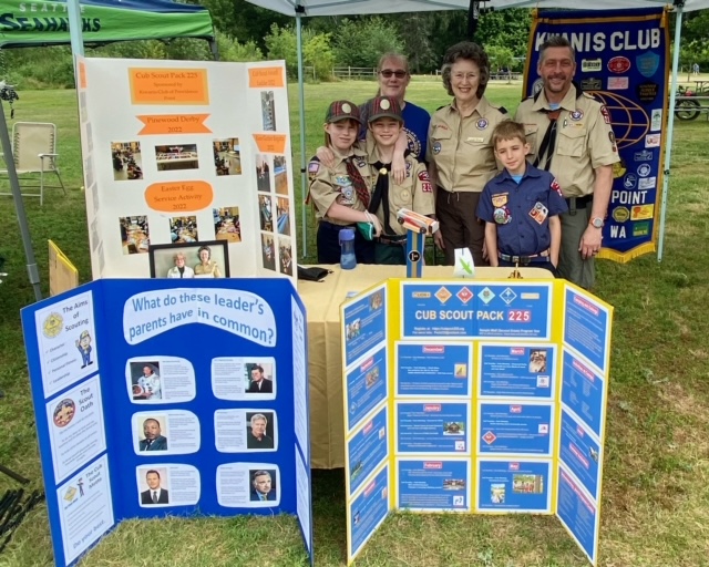 Cub Scouts and leaders in their booth at Lake Sammamish Parkadilly 2022. Display board show activities cubs are involved with. Kiwanis banner in background.