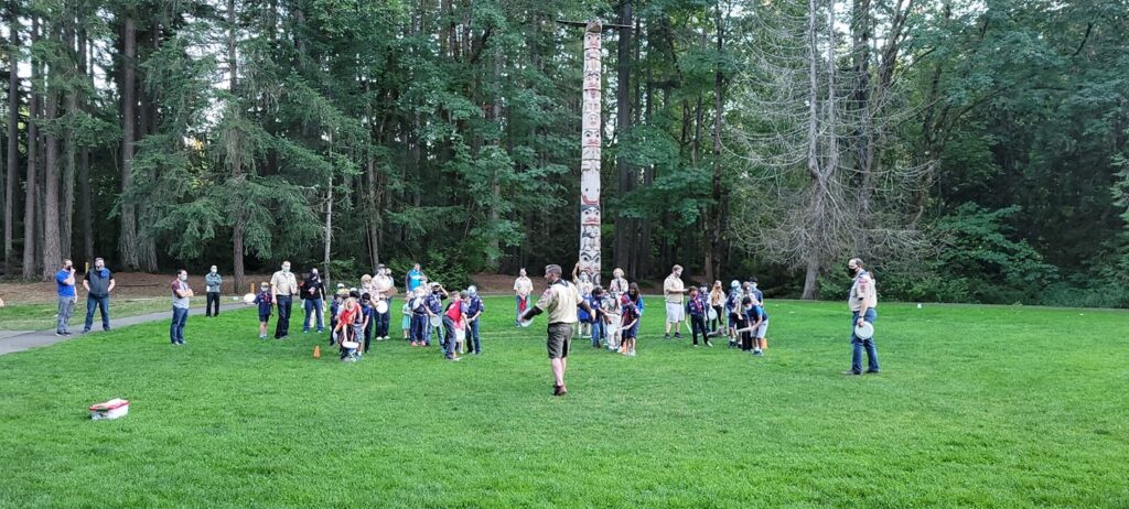 Cub Scouts lined up in field in front of woods. Leaders in front of the group of scouts.