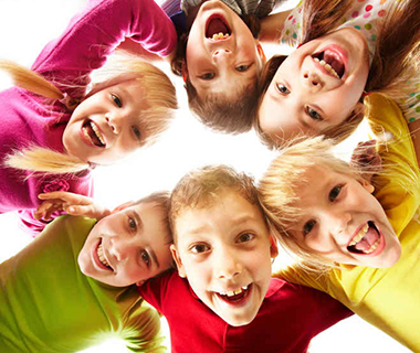 Children in a circle looking down at a camera and smiling. 