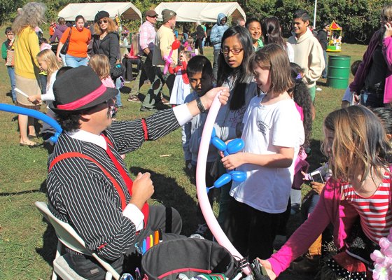 A performer in suspenders makes ballon animals in front of children.